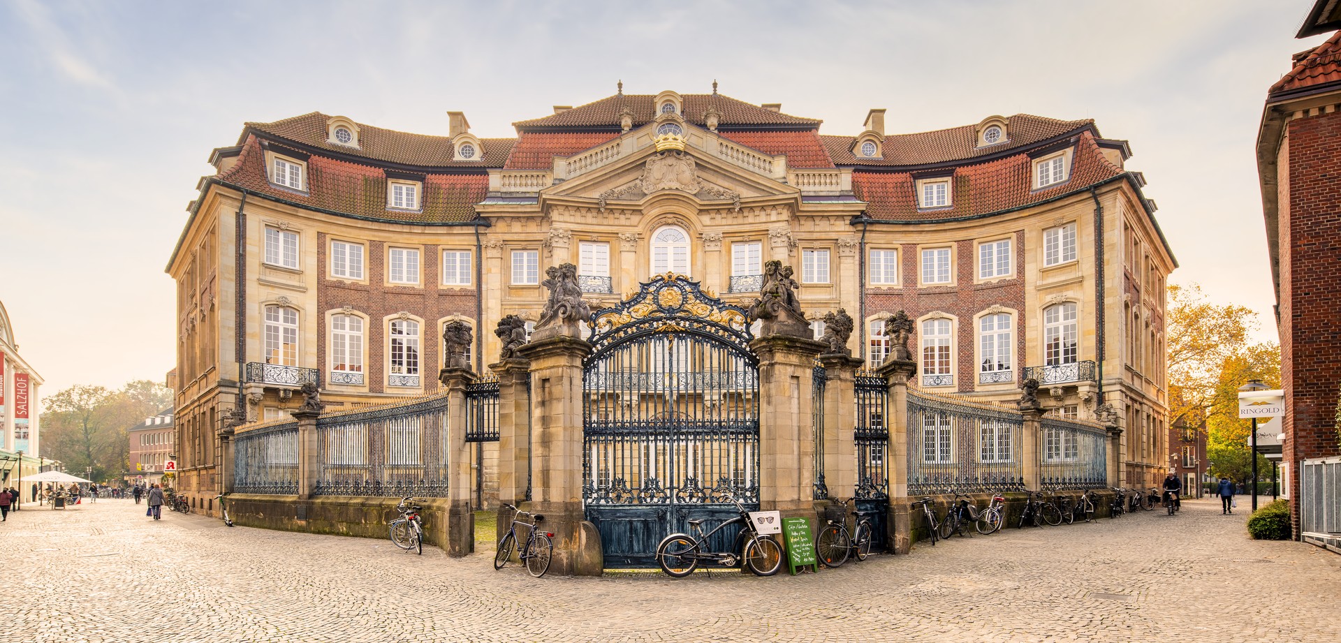 Erbdrostenhof in Münster von außen – barockes Adelspalais aus Sand- und Backstein, Vorplatz mit golden verziertem eisernem Zaun